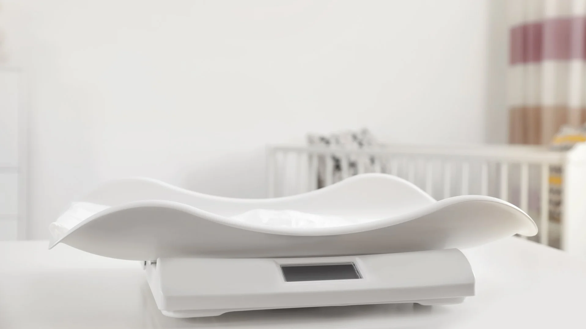 Babywaage mit ergonomischer Liegefläche und digitalem Display auf einem Tisch.