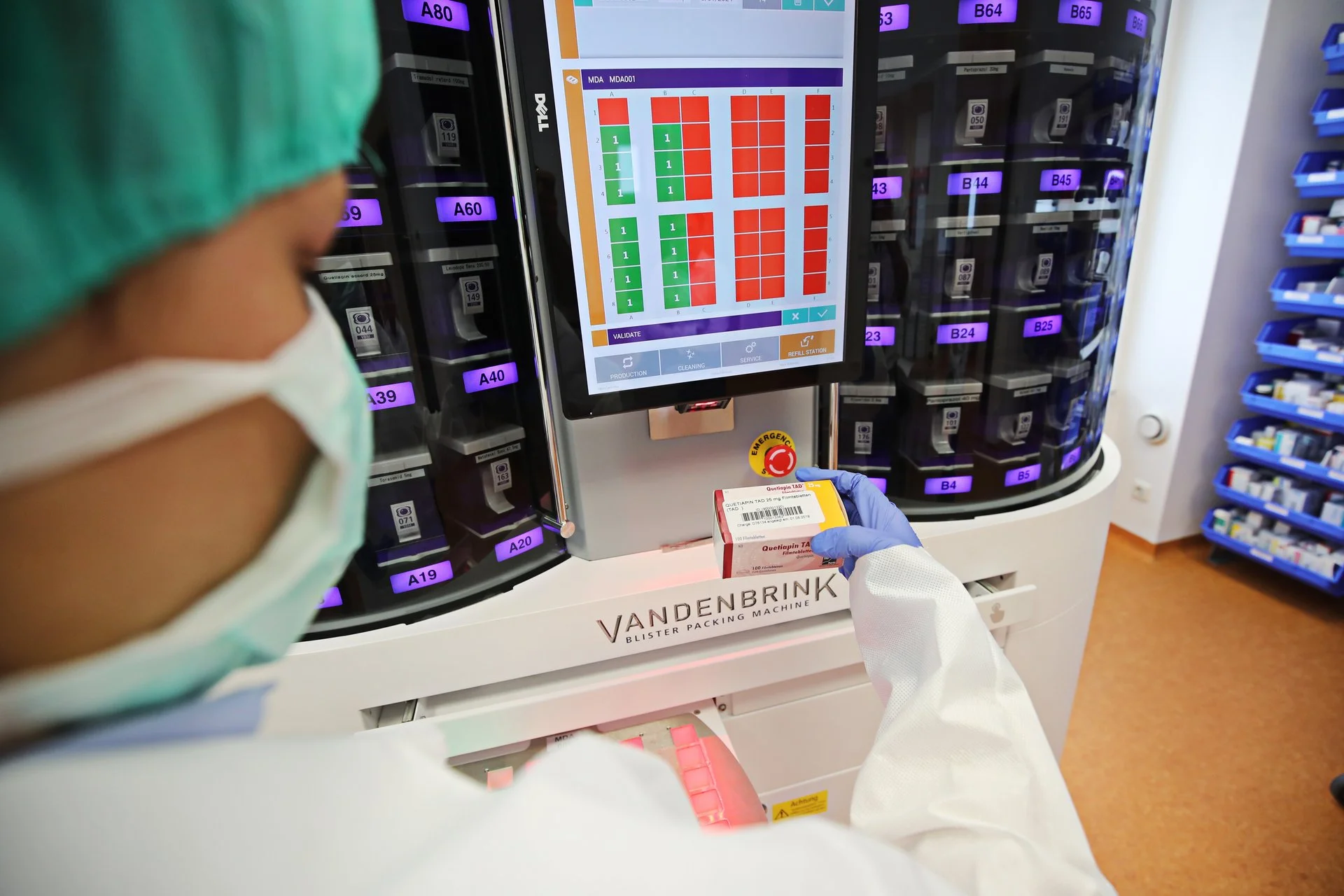 Mitarbeiterin mit Schutzkleidung bedient eine Verblisterungsmaschine und legt eine Medikamentenpackung ein; auf dem Display sind Produktionsdaten zu sehen.