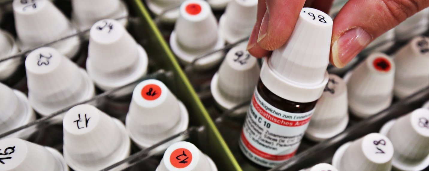 Hand nimmt ein beschriftetes Fläschchen aus einer Sortierbox mit vielen nummerierten Tropfflaschen in der Apotheke.