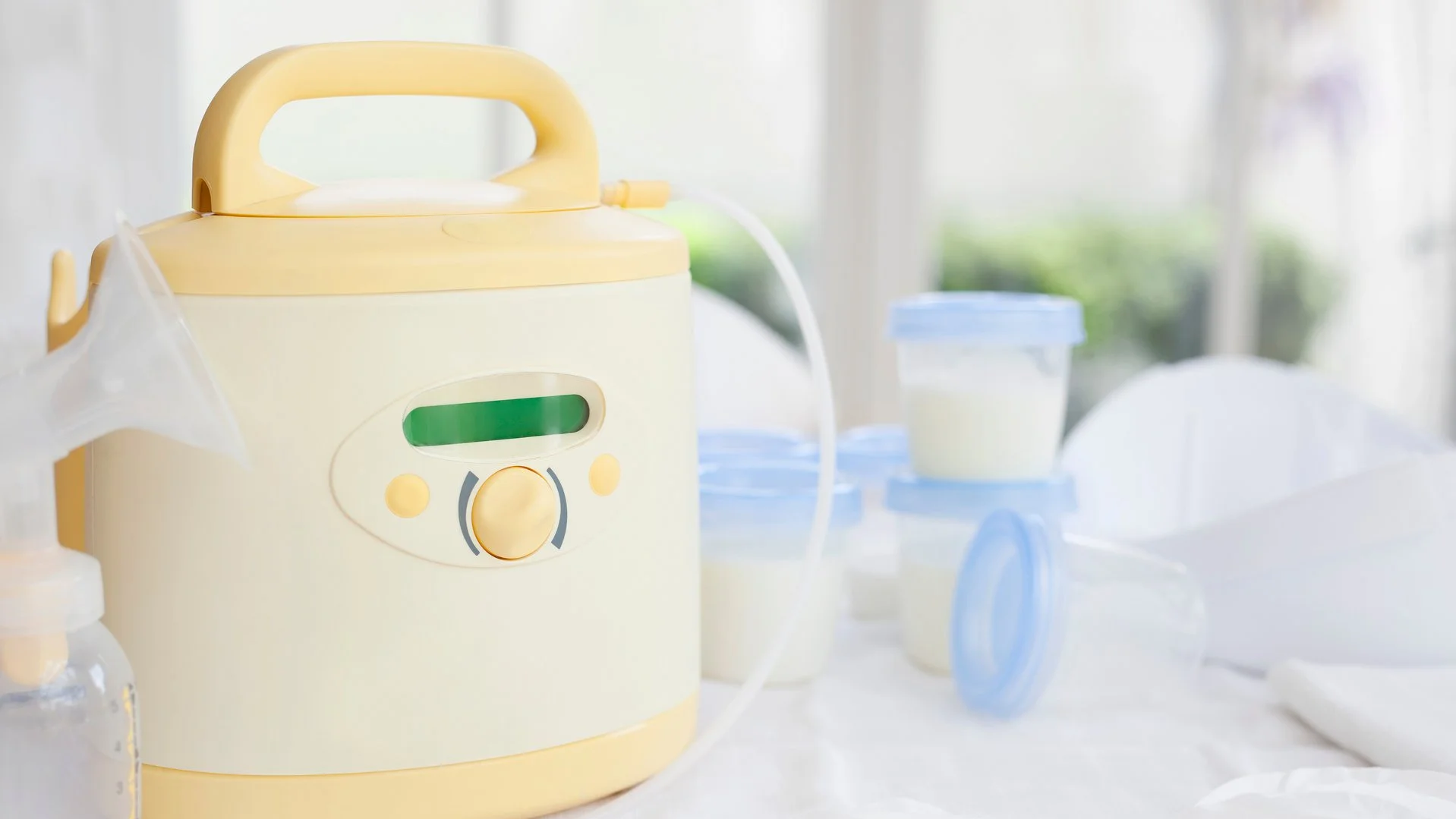 Elektrische Milchpumpe mit Zubehör wie Flaschen, Auffangbehältern und Deckeln auf einem Tisch.