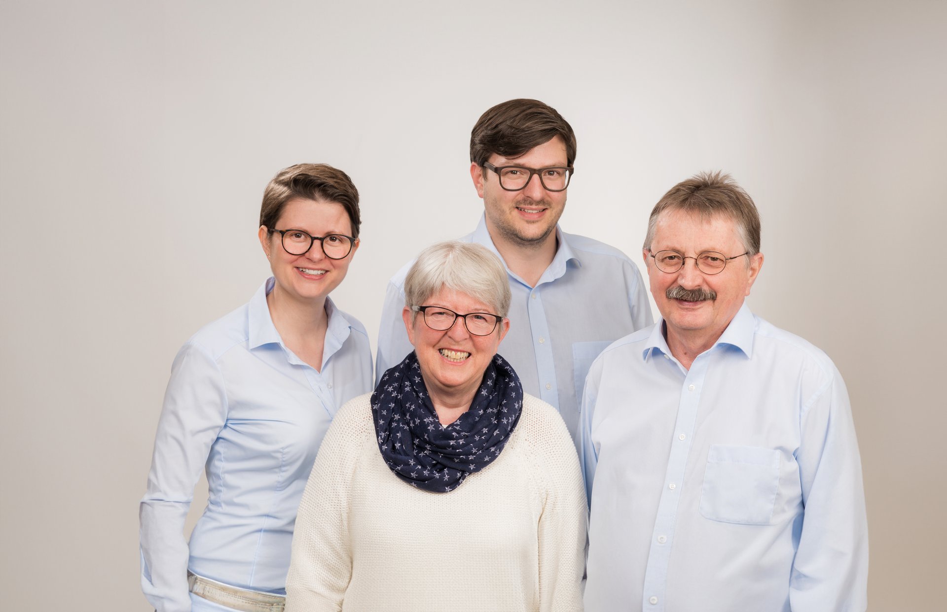 Gruppenfoto der Familie Scharpf: vier Personen stehen nebeneinander und lächeln vor hellem Hintergrund.